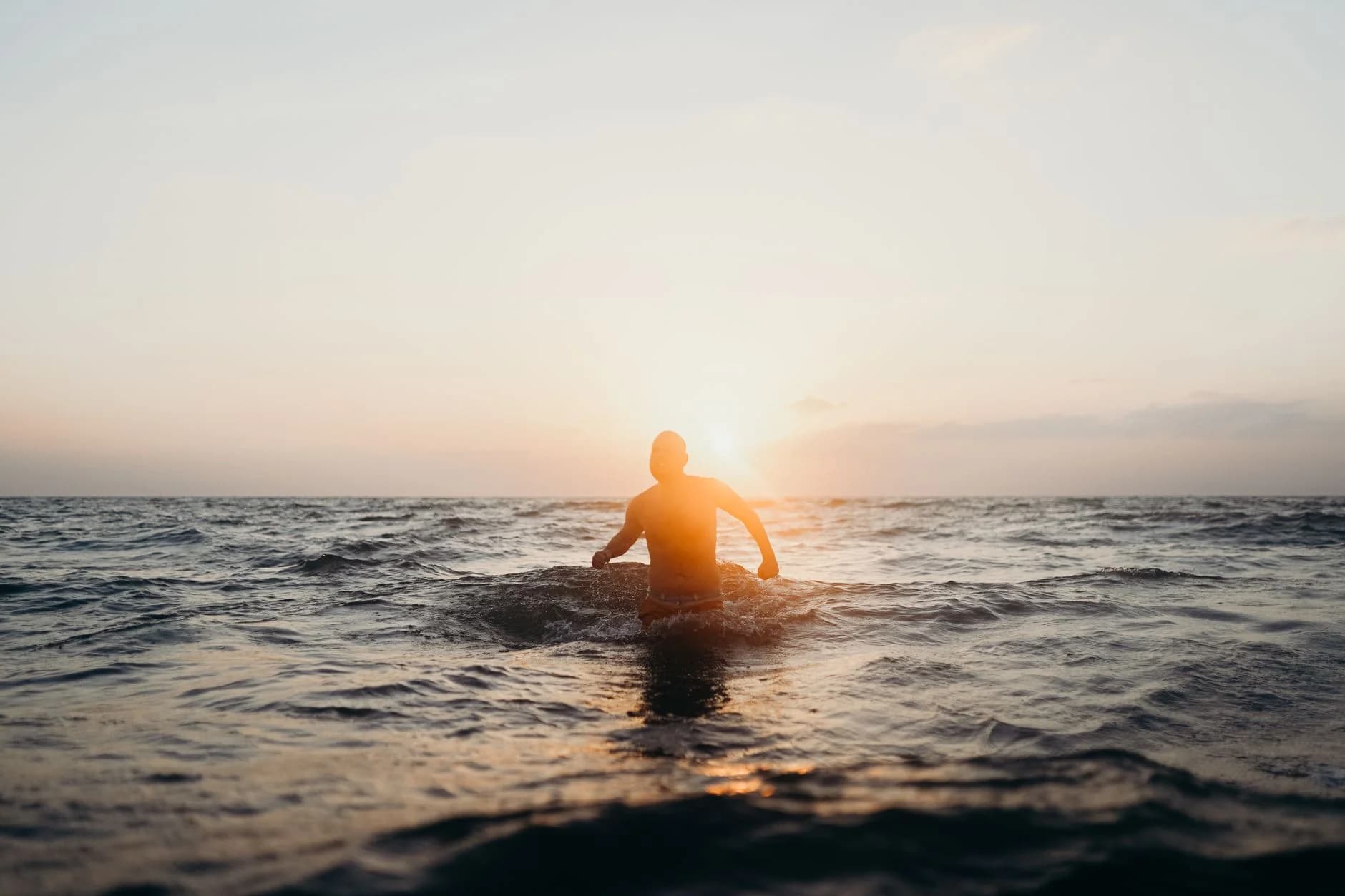 Triathlete wading into open water at sunset, silhouetted against the horizon.